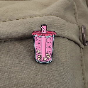 Detailed shot of an enamel pin featuring a pink juice cup with teeth on a canvas bag