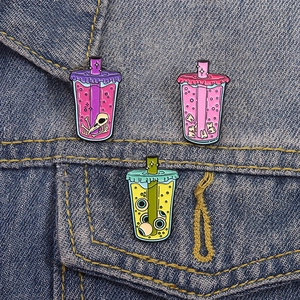 Quirky creative beverage cup brooches with eyeball and skull elements on denim jacket