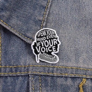Inspirational enamel brooch with motivational quote on denim jacket background