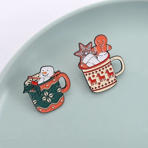 Christmas enamel pins featuring snowman and reindeer mugs on a ceramic dish