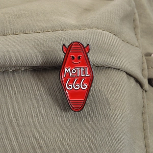 Detail of red Motel 666 enamel pin with devil horns on a green nylon bag strap