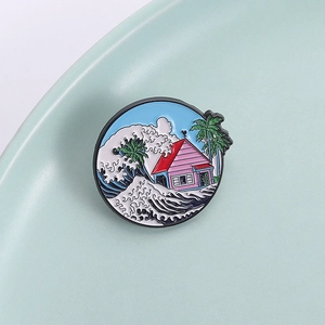 Round enamel brooch featuring pink house and sea waves on blue background