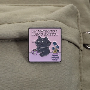 Detail of funny black cat enamel pin with Un Matecito Y Luego Existo text on canvas