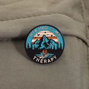 Close-up of hiking enamel pin on green fabric with Hiking Is My Therapy slogan