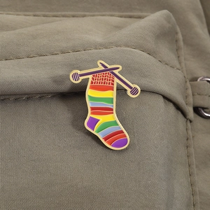 Detailed close-up of rainbow striped sock brooch with purple knitting needles on a canvas bag