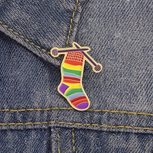 Rainbow knit sock enamel pin with purple needles on denim jacket collar