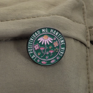 Artistic floral enamel brooch with positive Spanish quote on green textured fabric