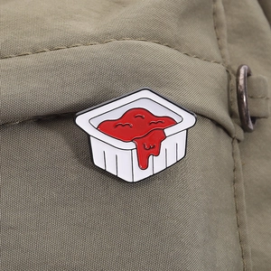 Detail of creative ketchup sauce enamel pin with red drips on green fabric texture