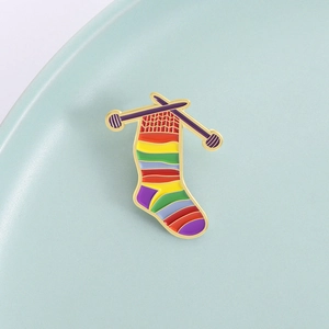 Rainbow knitted sock enamel brooch with crossover needles on light blue ceramic background