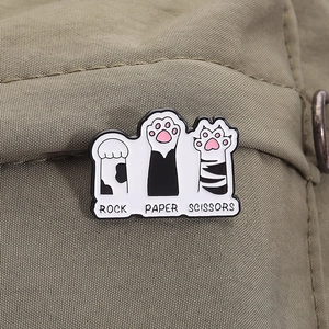 Macro detail of enamel cat paw pins featuring rock paper scissors on green fabric