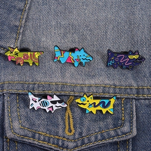 Detailed close-up of five colorful artistic puppy enamel pins on blue denim fabric