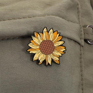 Detailed close-up of a sunflower enamel pin on olive green fabric with yellow petals