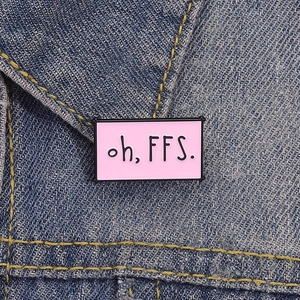 Broche en émail rose avec texte 'oh, FFS.' épinglée sur un col en jean bleu