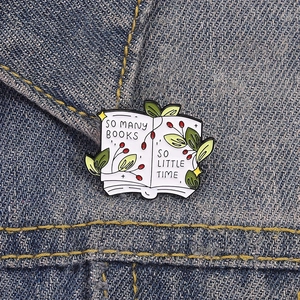Enamel book brooch with green leaves and So Many Books So Little Time quote on denim jacket