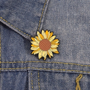 Detail of sunflower enamel pin with vibrant yellow petals on denim jacket texture