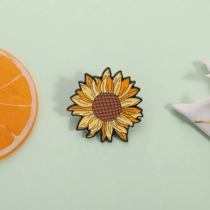 Sunflower enamel brooch with yellow gradient petals and brown center on soft green backdrop