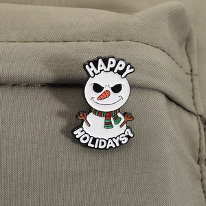 Detail of angry snowman enamel pin with Happy Holidays text on green canvas background