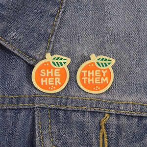 Pins émaillés orange avec pronoms SHE HER et THEY THEM sur tissu en jean bleu