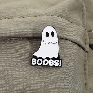 Macro shot of funny ghost enamel pin featuring Boobs text on beige canvas background