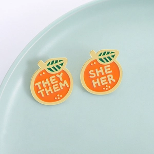 Pins émaillés en forme d'orange avec pronoms THEY THEM et SHE HER sur un plateau
