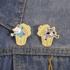 Close-up of enamel opossum and raccoon pins on dark blue denim fabric background