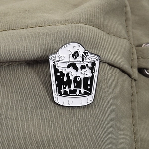 Detail of gothic enamel pin showing a skull melting in a glass on olive green fabric