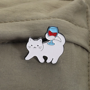 Makroaufnahme einer Emaille-Anstecknadel mit weißer Katze und Rotweinglas im Detail
