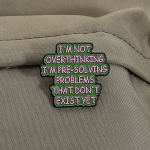 Detail of green enamel pin with pink funny overthinking quote on khaki canvas background