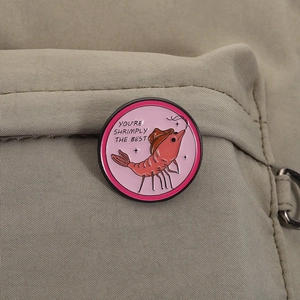 Détail d'un pin's rond en émail avec crevette et chapeau de cowboy sur un sac kaki
