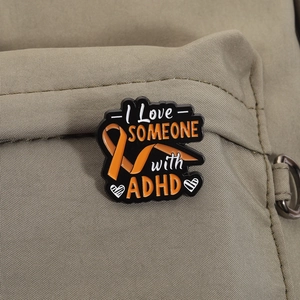 Detail shot of I Love SOMEONE with ADHD enamel pin on a canvas backpack surface