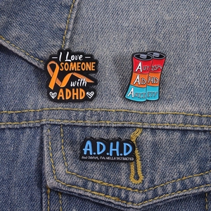 Cartoon ADHD enamel pins featuring orange ribbons and battery energy level designs
