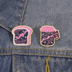 Detail of glittery cosmic jam jar and toast enamel pins on blue denim fabric