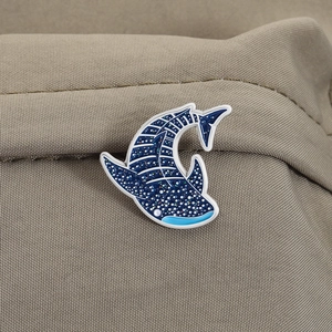 Detail of cartoon whale shark enamel pin with blue gradient and white spots on fabric