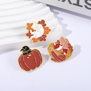 Three autumn enamel pins featuring a cat in maple leaf, fox, and crow in pumpkin designs