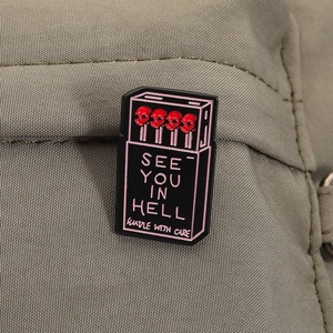 Close-up of gothic matchbox enamel pin with skull matches and 'See You In Hell' text