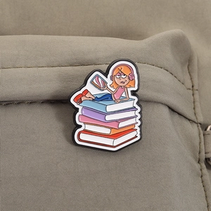 Gros plan détaillé d'un pin's en émail fille lisant sur des livres sur un sac à dos kaki