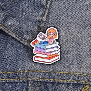 Vue rapprochée du pin's émaillé fille lisant des livres sur un tissu en denim bleu