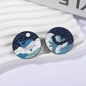 Enamel whale pins with starry sky and ocean wave designs on white background