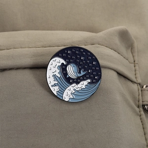 Detailed close-up of a whale and ocean wave enamel pin attached to a khaki canvas surface