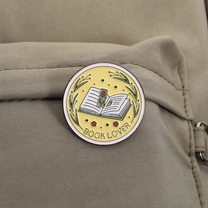 Detail shot of round Book Lover enamel pin with floral motifs on a khaki canvas backpack