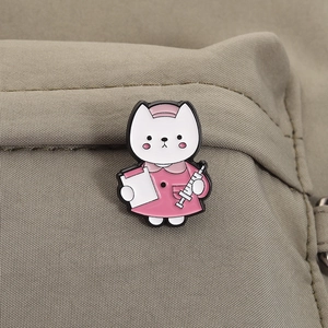 Close-up of a cute cat nurse enamel pin on khaki fabric with detailed syringe and folder