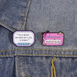 Detail of funny bookish enamel pins on a denim jacket featuring five stars and text