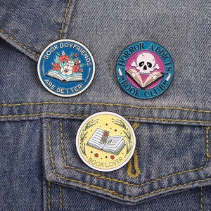 Close-up of three skull and book enamel pins pinned on a classic blue denim jacket pocket