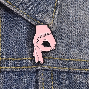 Macro d'une broche en émail rose motif main GOTCHA sur tissu en denim bleu