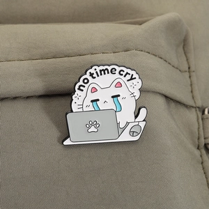 Detailed close-up of a crying cat enamel pin with a laptop on a khaki canvas fabric