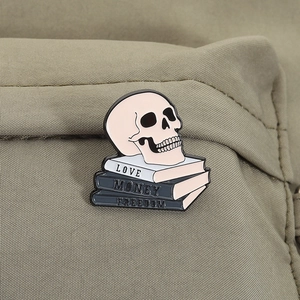 Detailed enamel pin with skull and books labeled Love, Money, Freedom on canvas fabric