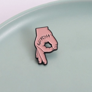Broche en émail rose geste de la main OK avec texte GOTCHA sur un plateau en céramique