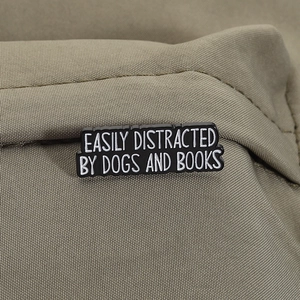 Close-up of enamel pin on canvas with text 'Easily Distracted by Dogs and Books'