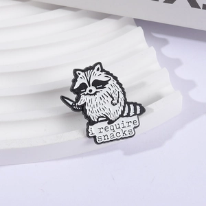 Funny raccoon enamel pin holding a knife with 'i require snacks' text on white display