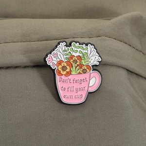 Macro shot of an enamel flower coffee cup pin with motivational text on olive canvas